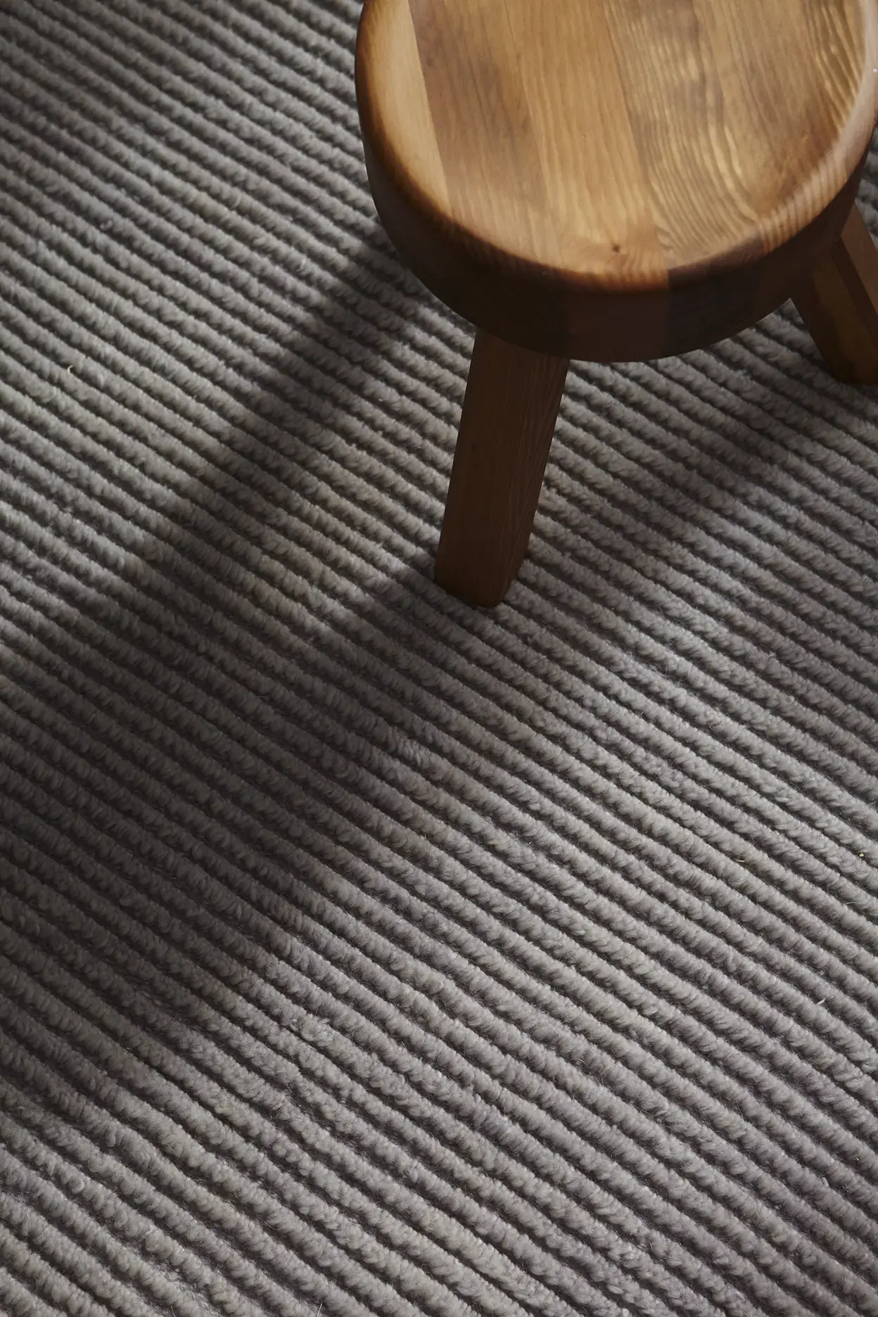 Nami Misty Sky rug texture close-up showing ribbed wool pattern with wooden stool