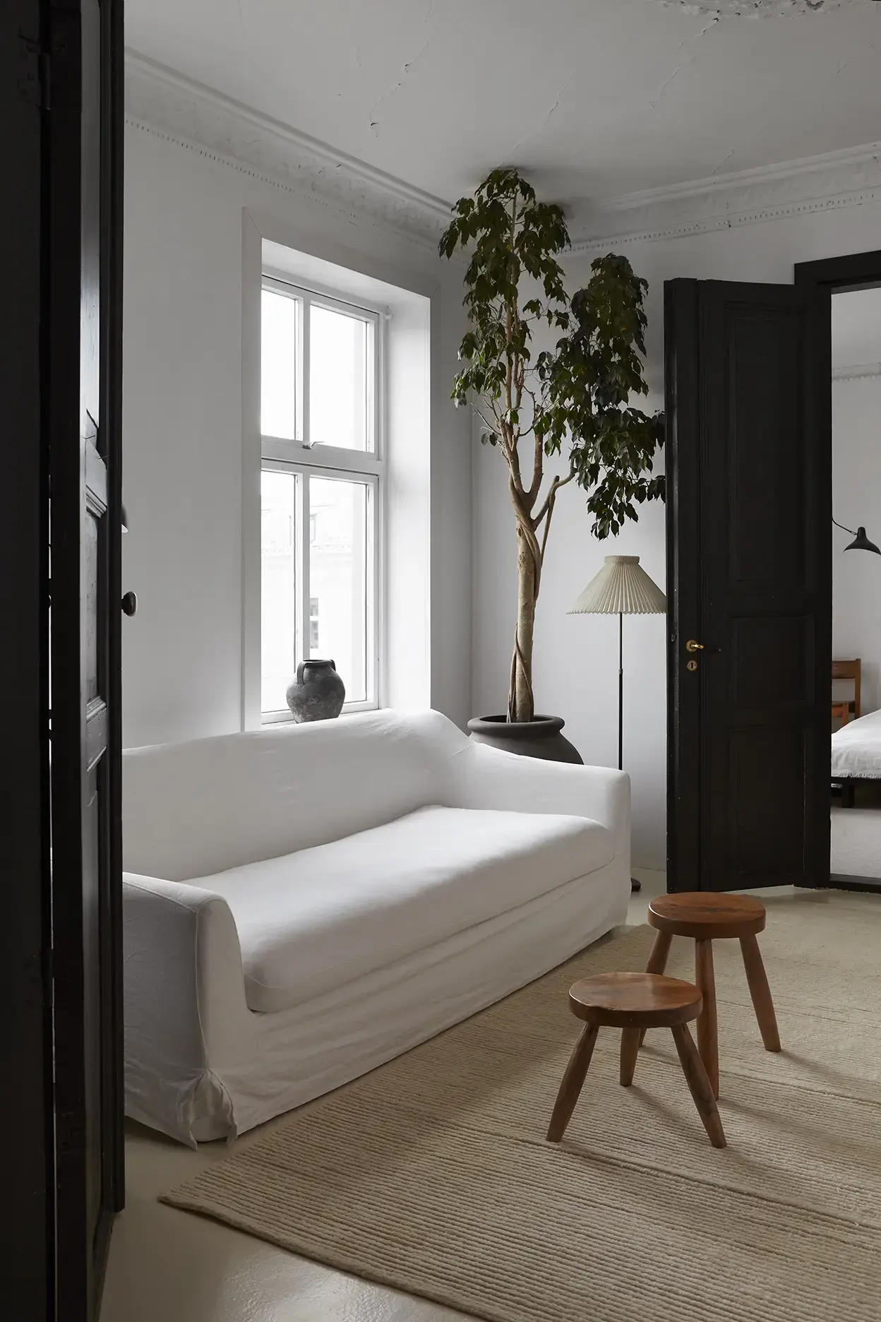 Nami Sand rug in a bright living room with white sofa and wooden stools